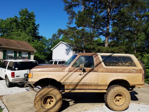 1988 Ford Bronco - Mud-covered 1988 Ford Bronco with large tires, parked next to a white SUV.