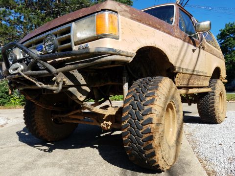 1988 Ford Bronco - This heavily modified Ford Bronco is covered in mud, suggesting recent off-road use.