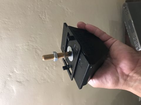 1997 Dodge 3500 - A black mounting bracket with a threaded bolt and nut is held in a person's hand against a textured wall.