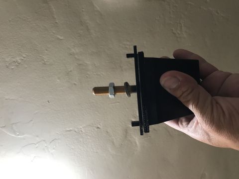 1997 Dodge 3500 - A black metal bracket with a bolt and nut is held by a hand against a textured wall.