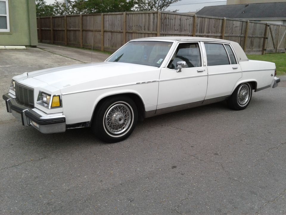 white sedan parked on asphalt, wooden fence behind it