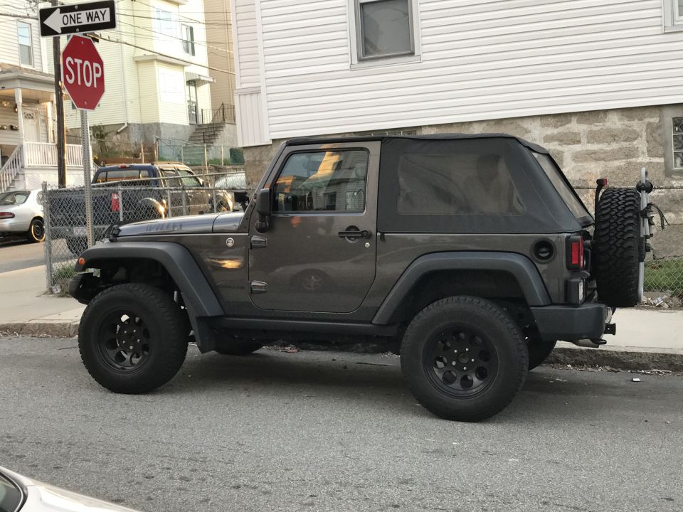 Gray two-door Jeep Wrangler with soft top parked on an urban street next to a stop sign