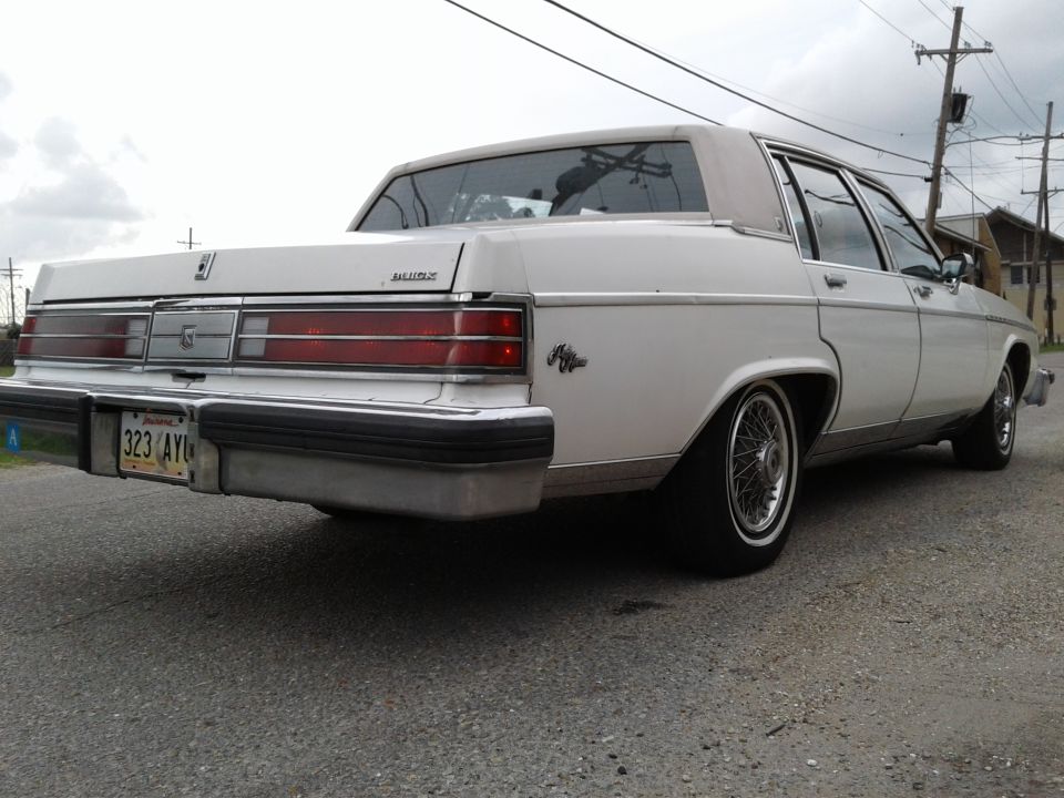 rear view of a white 1980s sedan with wire wheels and a license plate reading 323 AYI