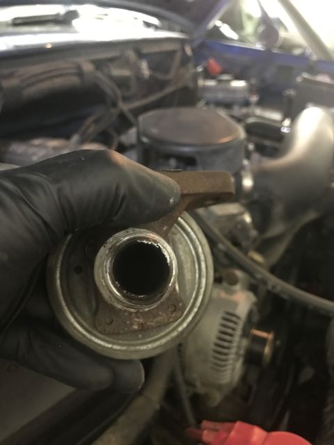 1996 Ford Bronco - A person holds an EGR valve, with the engine bay of a vehicle visible behind it.