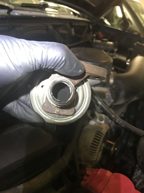 1996 Ford Bronco - A dirty EGR valve is held by a gloved hand, with engine components visible in the background.