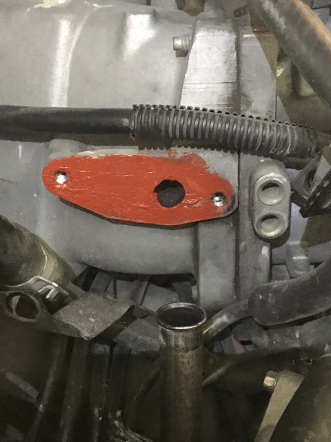 1996 Ford Bronco - Close-up of an EGR valve gasket, showing its mounting holes and red painted surface.