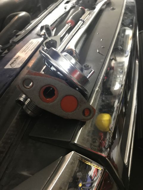 1996 Ford Bronco - A close-up view of an EGR valve and various tools resting on the engine compartment of a vehicle.