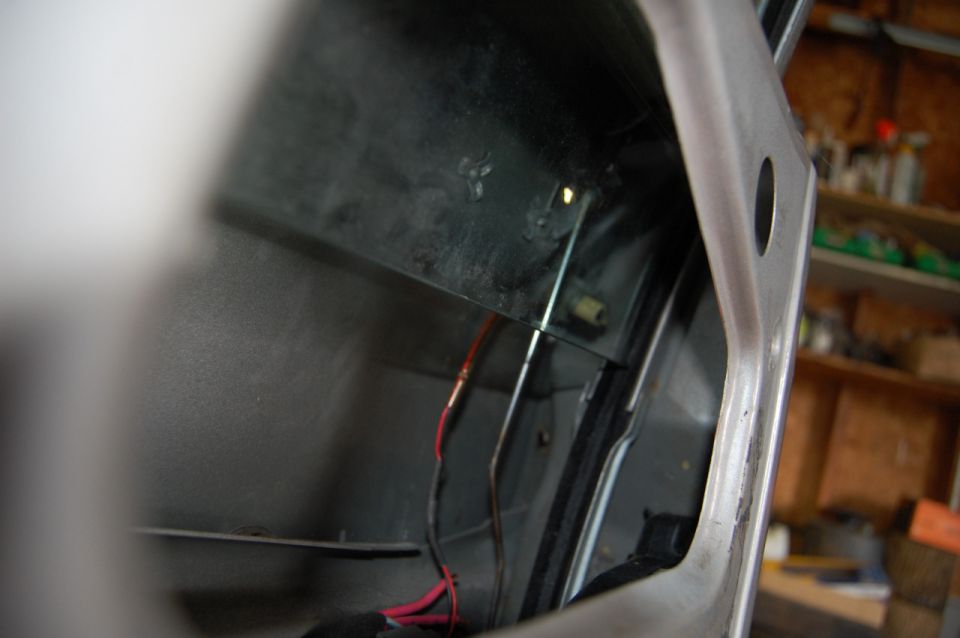 Car door panel interior with exposed red and black wires, metal frame, and black plastic trim
