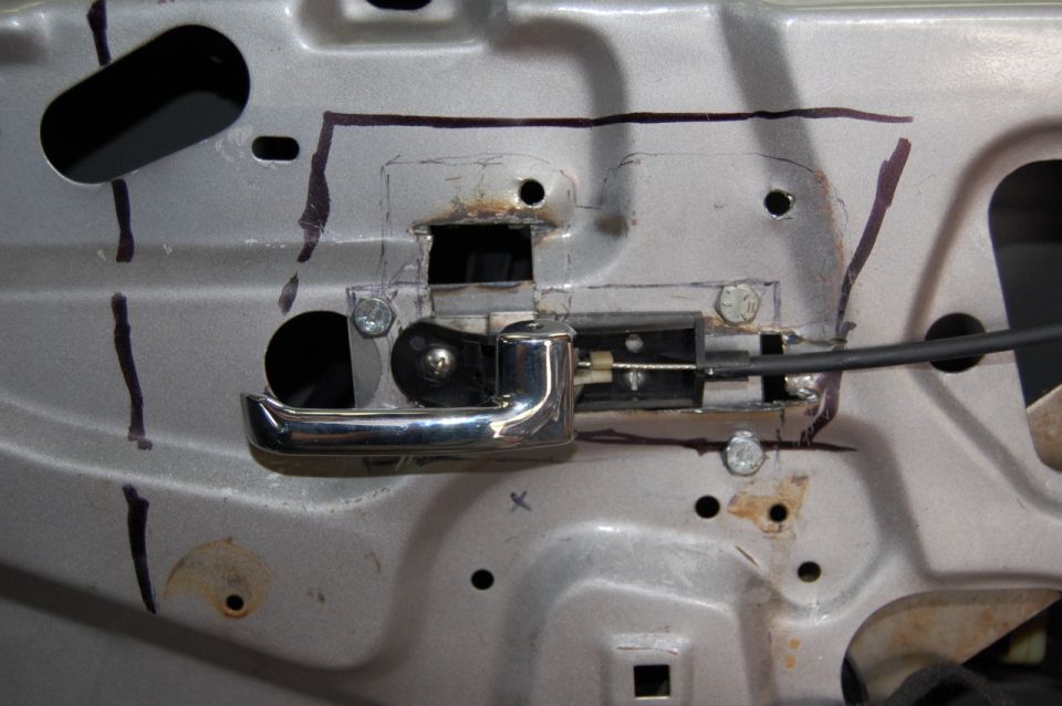 Close-up of a car's interior door panel showing the door handle mechanism and linkage. Markings are visible on the metal
