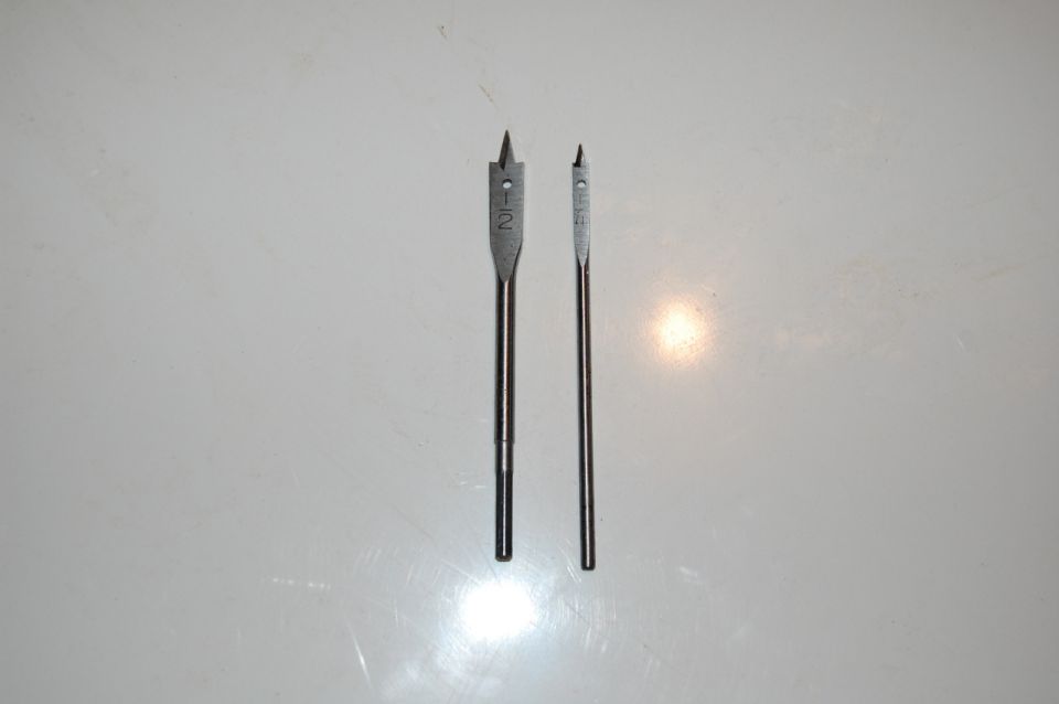 Two spade drill bits, one marked 1-1/2, on a white surface