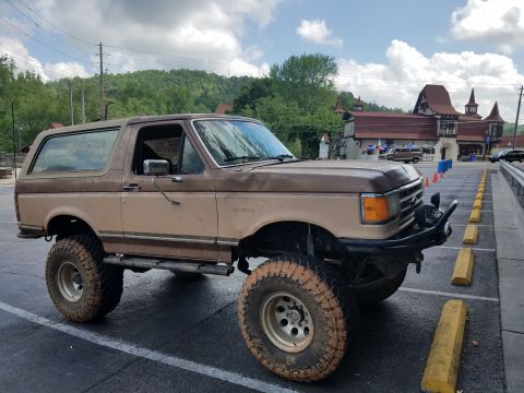 1988 Ford Bronco - This lifted Ford Bronco, likely from the late 1980s, is parked in a lot with a distinctive building in the background.