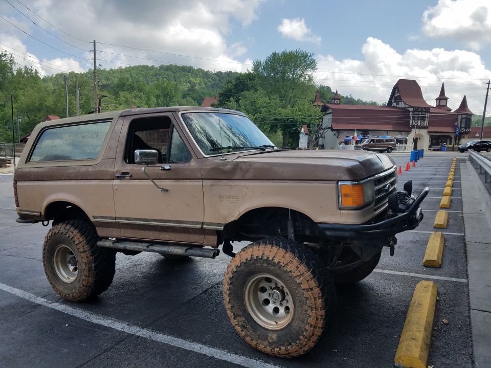 Brown lifted Ford Bronco with aftermarket bumper and large tires parked in a lot