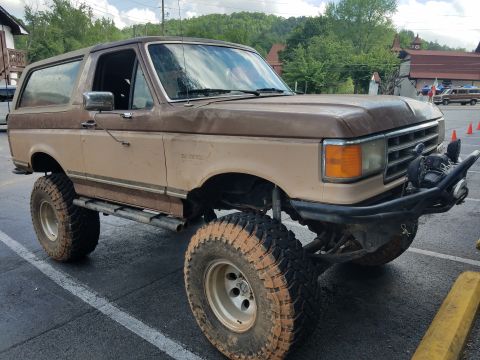 1988 Ford Bronco - This modified SUV features a two-tone brown paint scheme, aggressive off-road tires, and a heavy-duty front bumper.