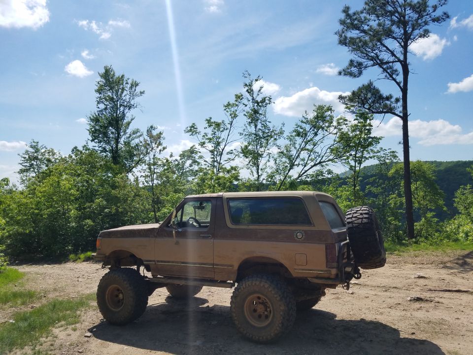 Brown Ford Bronco with lifted suspension and spare tire mounted on rear, parked on dirt road