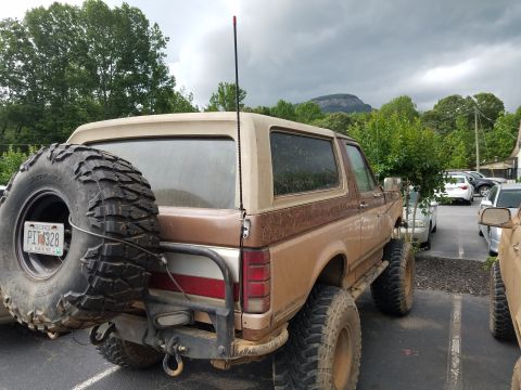 1988 Ford Bronco - This lifted Ford Bronco is parked in a lot with other vehicles visible in the background.