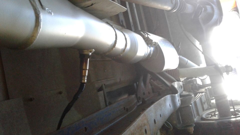 Exhaust pipe with an oxygen sensor attached, viewed from underneath a vehicle