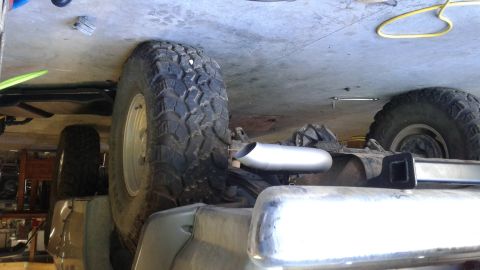 1985 Ford Bronco - Close-up view of a vehicle's undercarriage, focusing on the exhaust system and a large tire.