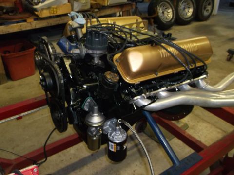 1964 Ford Galaxie - Engine assembly with gold valve covers and silver exhaust headers is mounted on a stand.