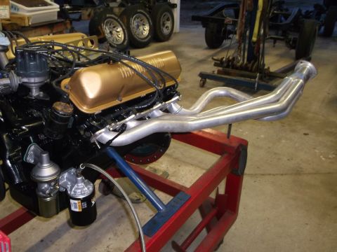 1964 Ford Galaxie - Engine assembly with gold valve covers and custom exhaust headers, mounted on a red engine stand.