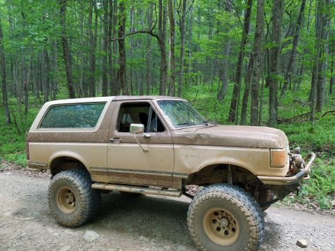 1988 Ford Bronco - A lifted 1987 Ford Bronco is parked on a dirt road surrounded by trees.