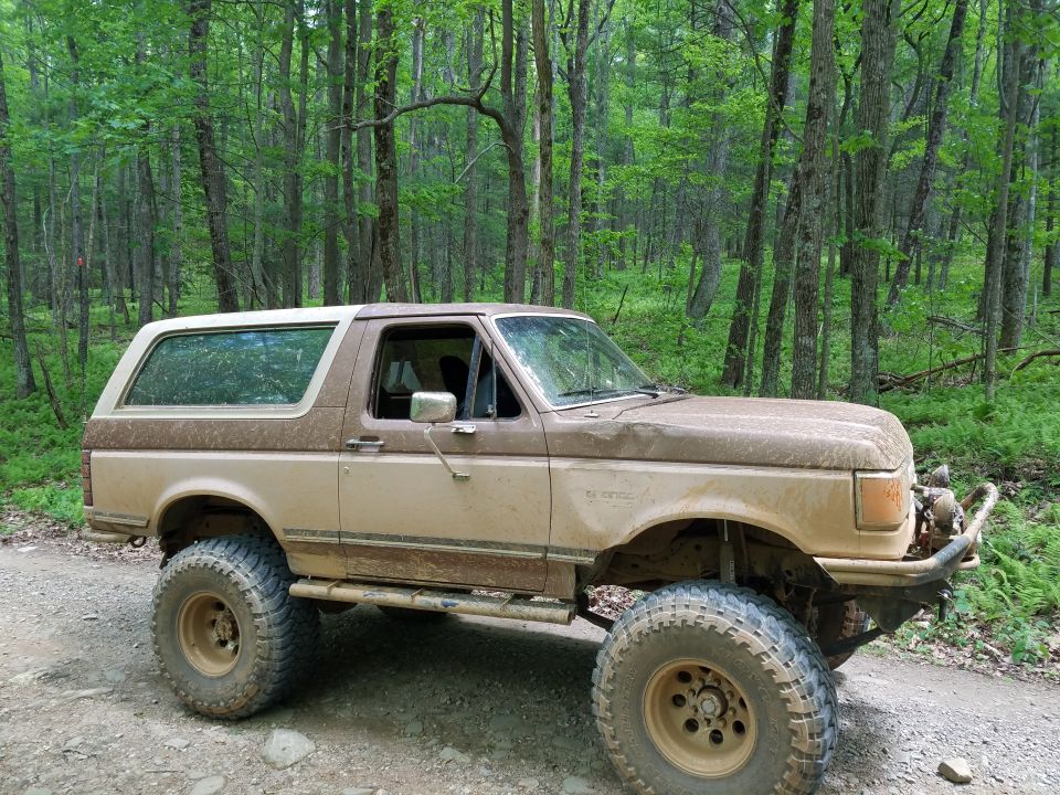Brown lifted Ford Bronco with off-road tires on a dirt road