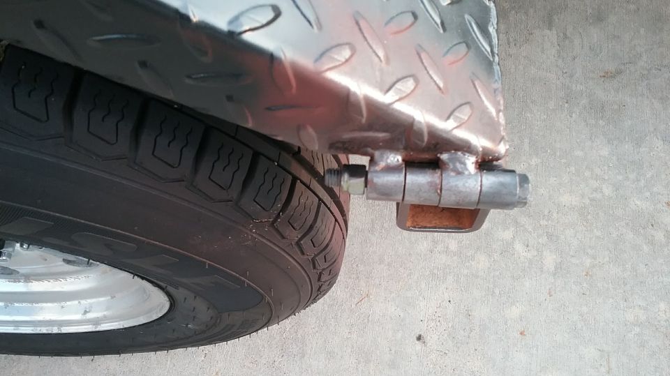 Close-up of a trailer's diamond plate fender and tire, showing a hinge mechanism