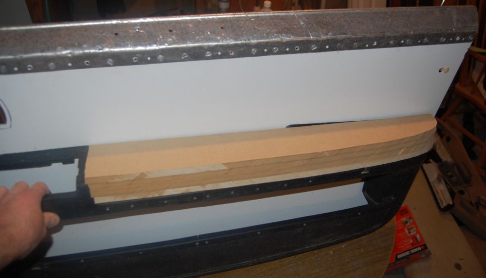 Car door panel with a piece of wood trim being fitted. A hand is visible on the left