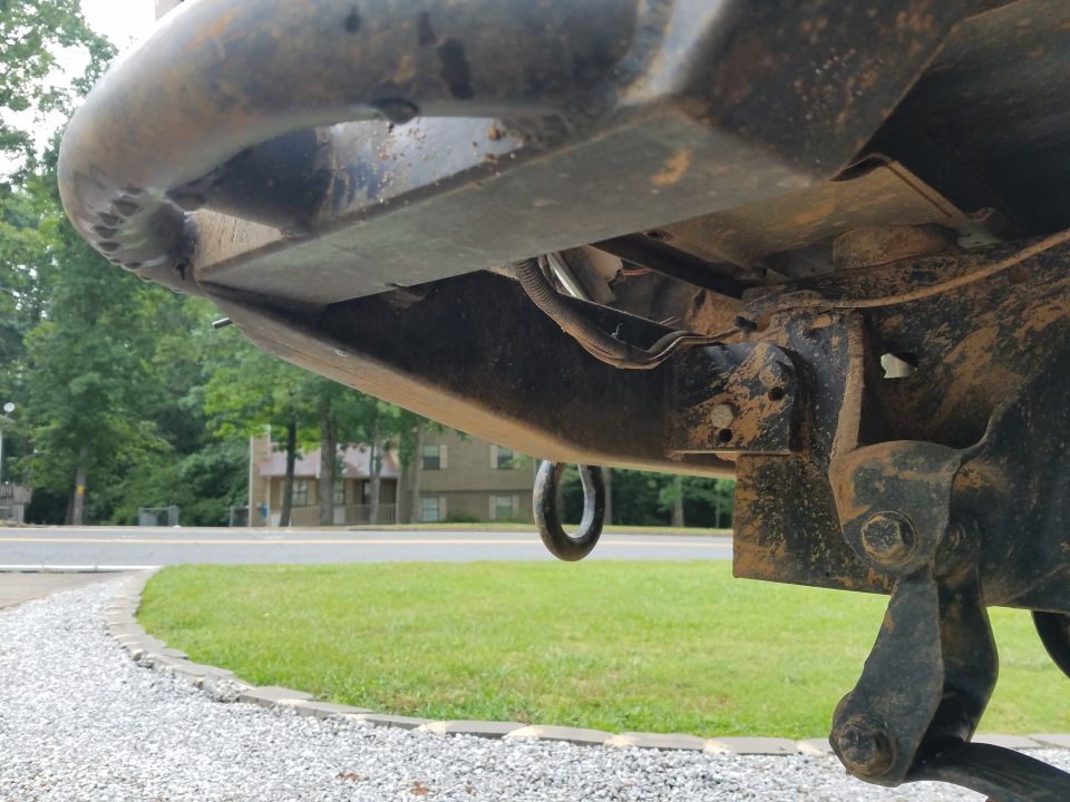 Undercarriage of a dirty vehicle with a tow hook and visible wiring