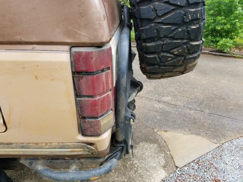 1988 Ford Bronco - Close-up of the rear corner of a brown SUV, showing the taillight and a mounted spare tire.