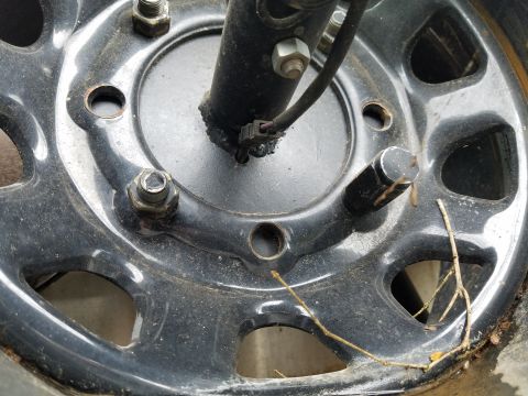 1988 Ford Bronco - Detail of a vehicle's wheel and brake caliper, showing the lug nuts and part of the suspension.