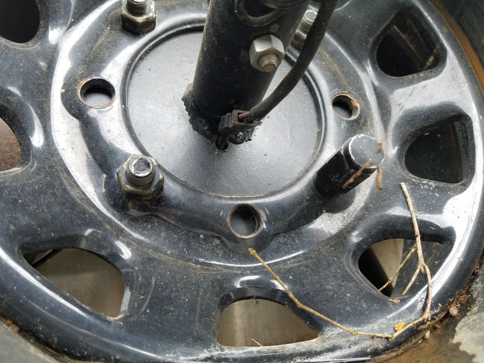 Close-up of a black wheel with five lug nuts and a black brake caliper