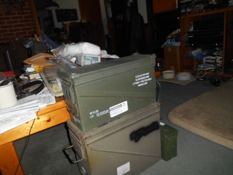 1972 Ford Bronco - A cluttered room with two green ammo cans stacked on top of each other in the foreground. A wooden table with papers and other items is to…