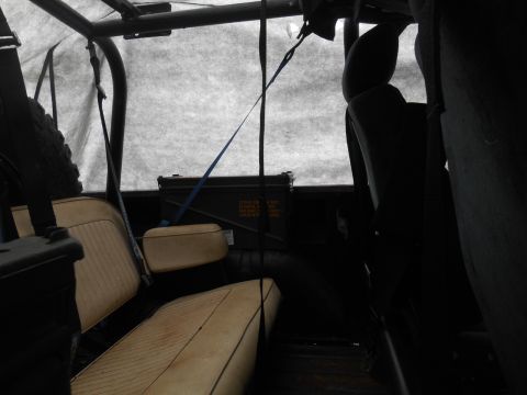 1972 Ford Bronco - The interior of a classic Ford Bronco shows tan vinyl seats and a dark green ammo can secured with a blue strap. A spare tire is visible on…