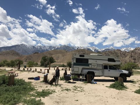 1997 Dodge 3500 - A white Dodge 3500 pickup truck with a camper shell is parked in a campsite with a woman and her dog standing nearby. Snow-capped mountains…