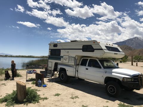 1997 Dodge 3500 - A white pickup truck with a camper shell is parked near a lake, with a person and a dog nearby.