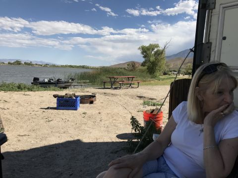 1997 Dodge 3500 - A woman relaxes at a campsite by a lake, with a boat moored nearby and a picnic table nearby.