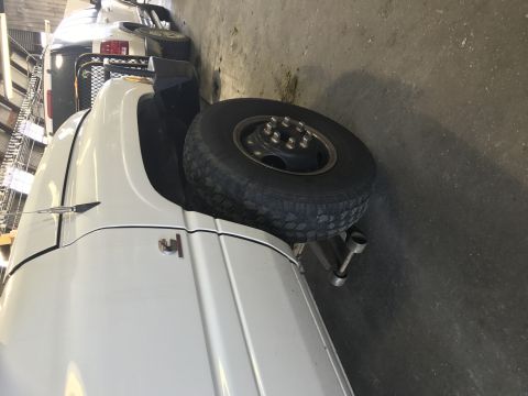 1997 Dodge 3500 - A white pickup truck is parked indoors, with its rear wheel elevated on a jack. Another white pickup truck is visible behind it.