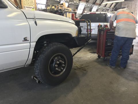 1997 Dodge 3500 - A white Dodge pickup truck is parked in a garage with a mechanic working on a toolbox next to it. The front passenger side wheel and fender…