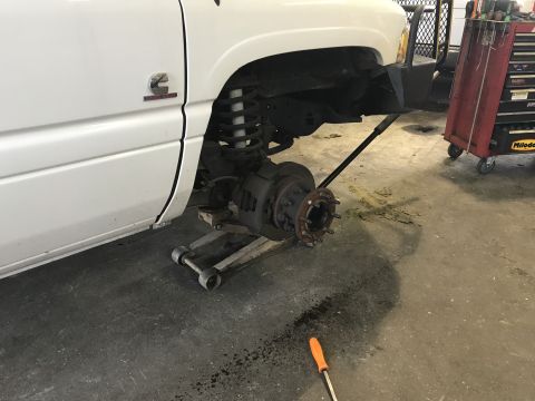 1997 Dodge 3500 - A white pickup truck is elevated on a jack with the front wheel removed, revealing the brake rotor and hub assembly. A red toolbox is visib…