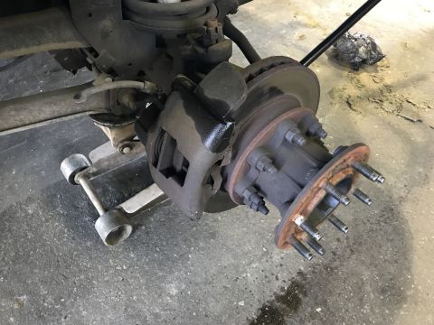 1997 Dodge 3500 - A close-up view of the front wheel hub assembly and brake caliper of a Dodge 3500, supported by a floor jack. The wheel studs are visible o…