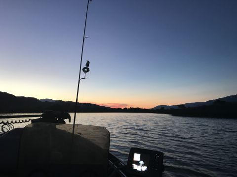 1997 Dodge 3500 - The image shows a fishing rod and a fish finder on a boat at dusk. The boat is on a body of water with hills in the background.
