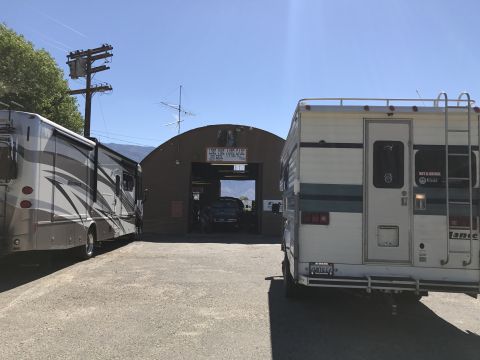 1997 Dodge 3500 - Two RVs are parked outside a large arched building with a sign that reads "LOVE FINE AUTO CARE". A dark colored car is visible inside the b…