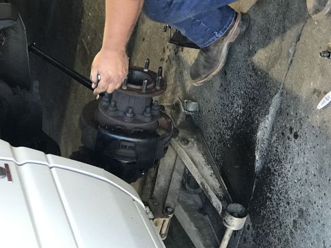 1997 Dodge 3500 - A person is using a long-handled wrench to tighten lug nuts on the front hub of a large truck. The vehicle's white fender is visible in the…