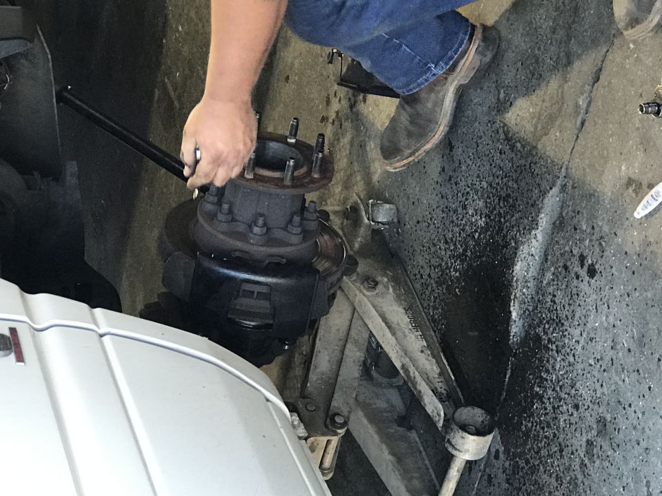 Mechanic tightening lug nuts on a large truck's front hub with a long wrench.
