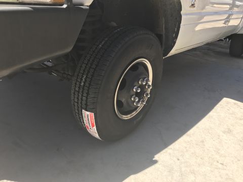1997 Dodge 3500 - Close-up of the front passenger-side dually wheel and tire on a white Dodge 3500 pickup truck. A red and white tire sticker is visible on t…