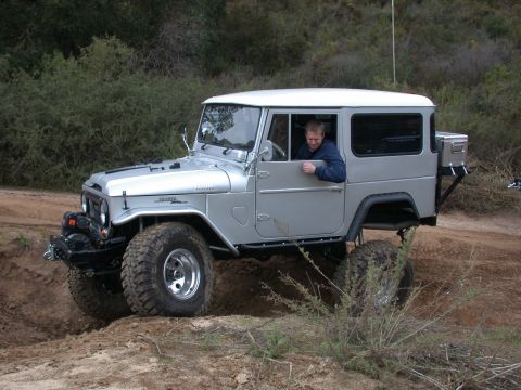 1996 Ford Bronco - A silver Toyota Land Cruiser FJ40 navigates rough terrain with a driver inside.