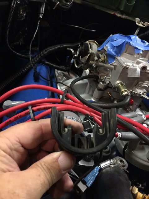 1978 Ford Bronco - A person's hand holds a black plastic part with two U-shaped openings in front of a vehicle engine bay. The engine features red spark plug…