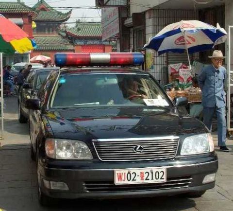 1998 Ford Crown Victoria - A black Lexus sedan, likely a police vehicle, is parked on a street with traditional Chinese architecture in the background.