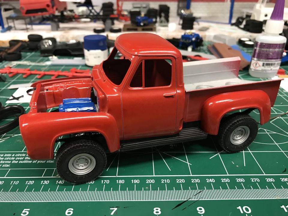 Red model pickup truck with open hood showing blue engine on a green cutting mat.