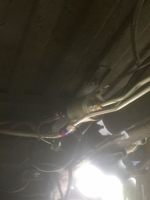 1974 Ford Bronco - Underneath view of a vehicle's fuel filter assembly, showing braided fuel lines connected to a cylindrical filter. The assembly is mounted…